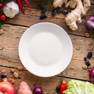 Flat lay, vegetables on a wooden background and an empty white plate.